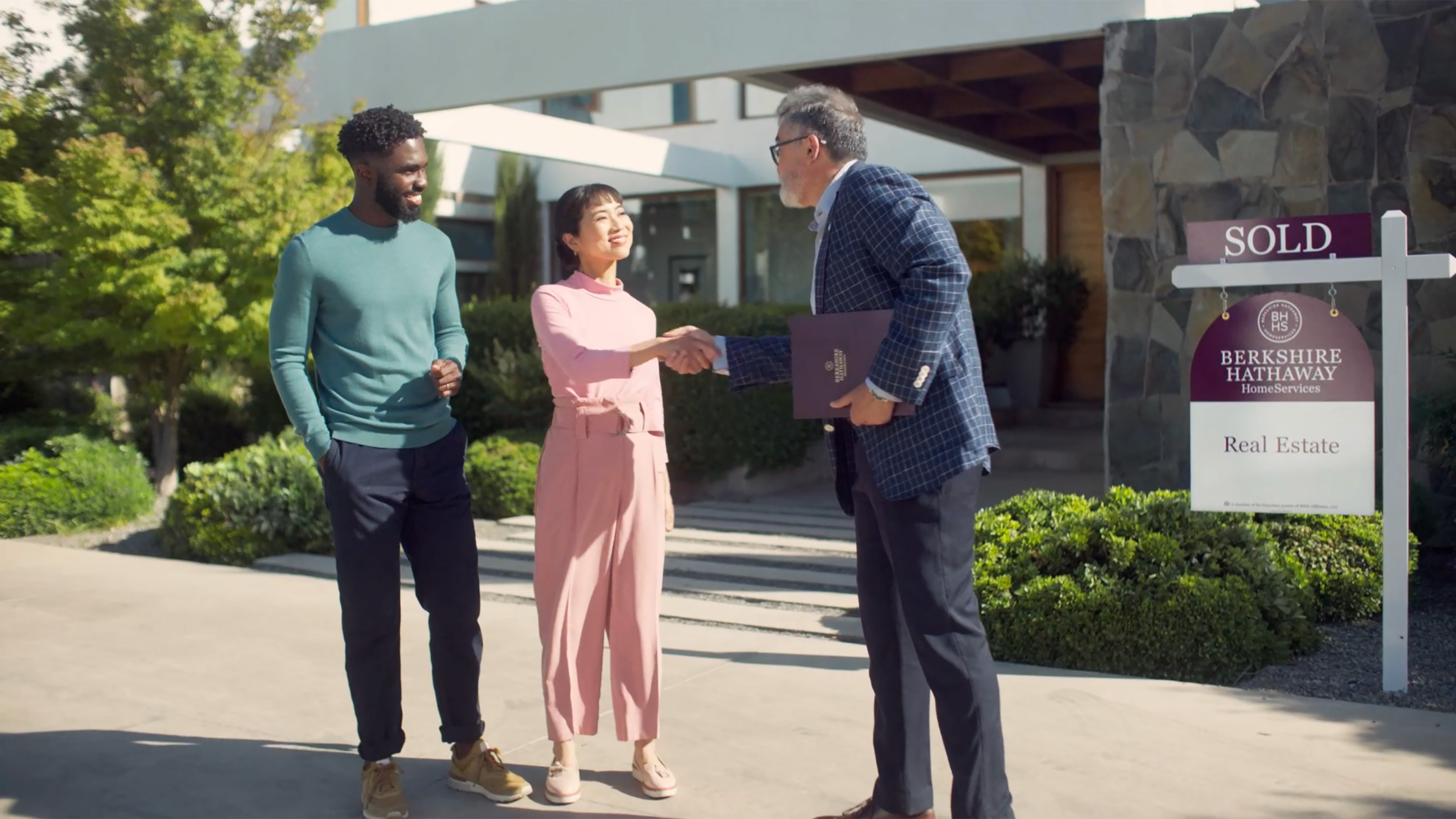 Real estate agent greeting mixed race couple in front of house for sale
